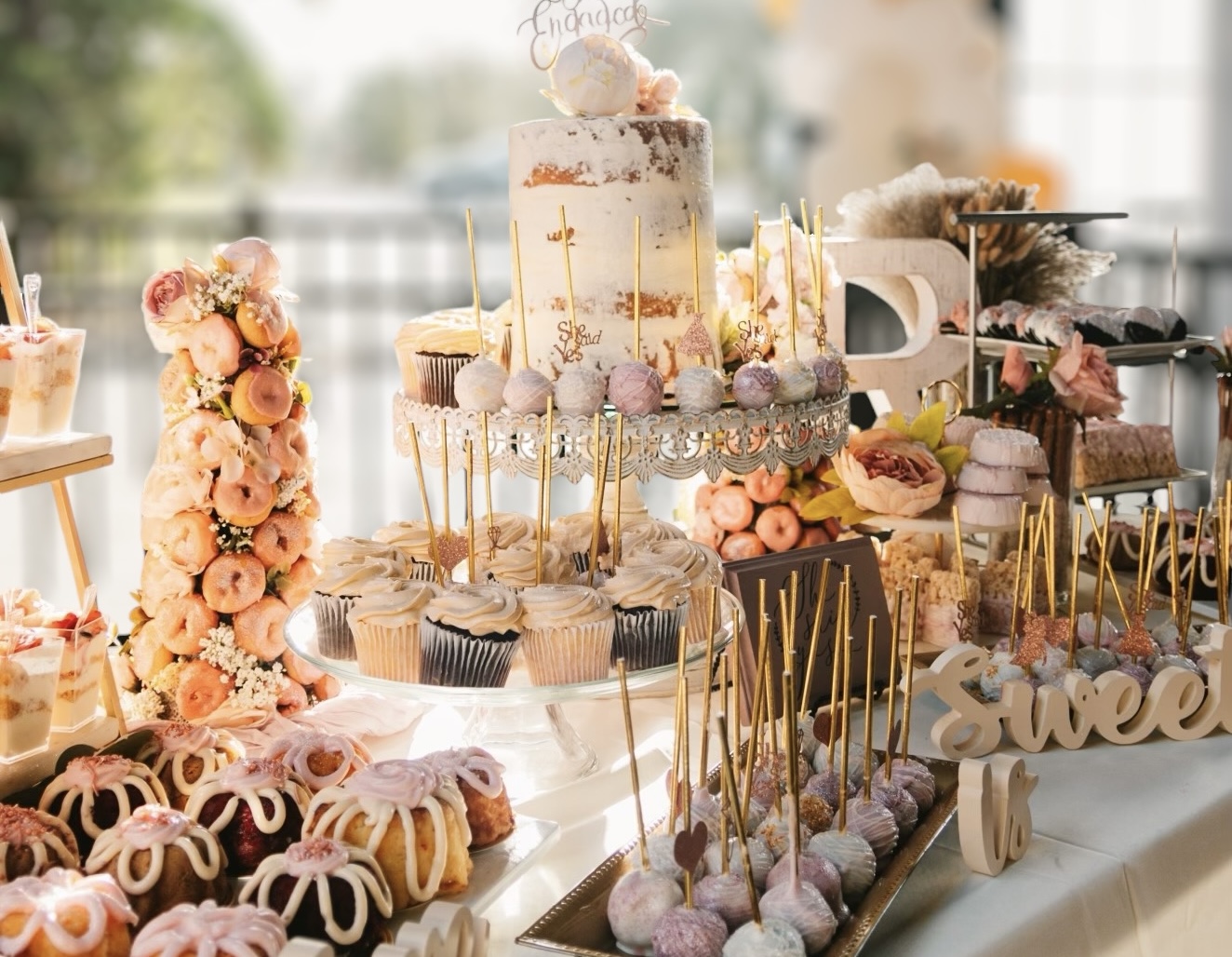 Sugar and Grace Sweets dessert spread — tiered cake, donut tower, cake pops with gold accents and styled florals.