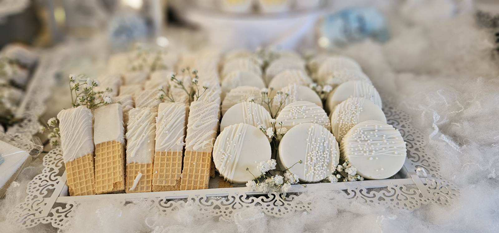 Wide horizontal tray of white-glazed wafer cookies and chocolate-covered Oreos accented with baby's breath.