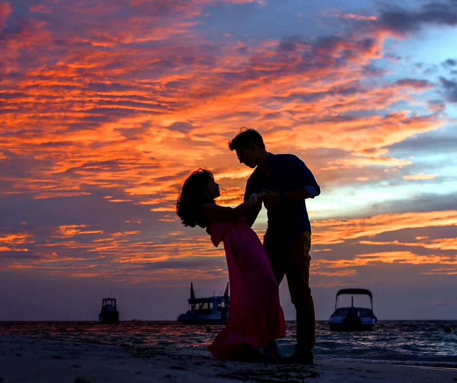 A couple sharing a quiet moment on the beach beneath a colorful sunset.