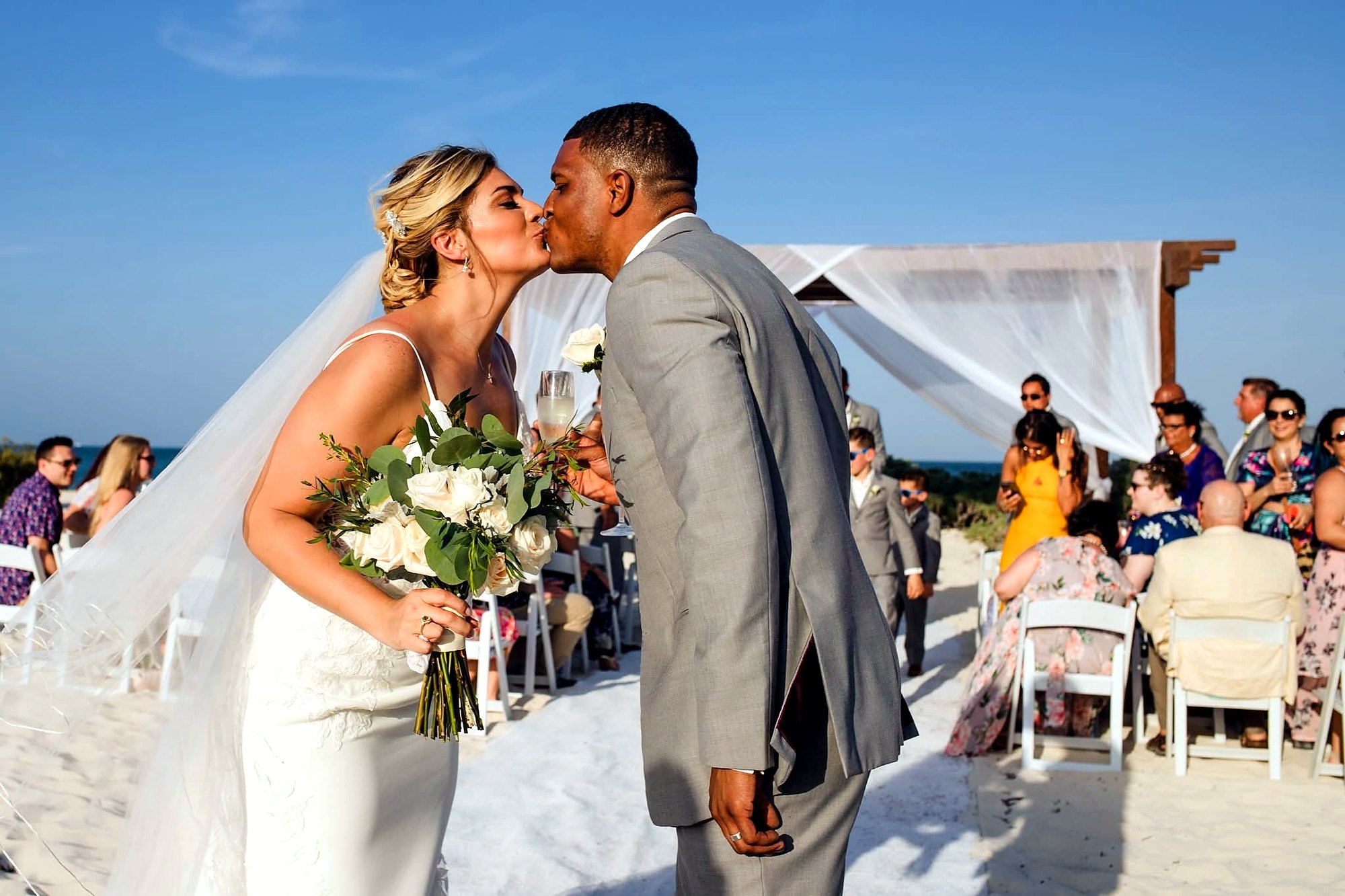 A wedding couple celebrating beside a ceremony arch overlooking the sea.