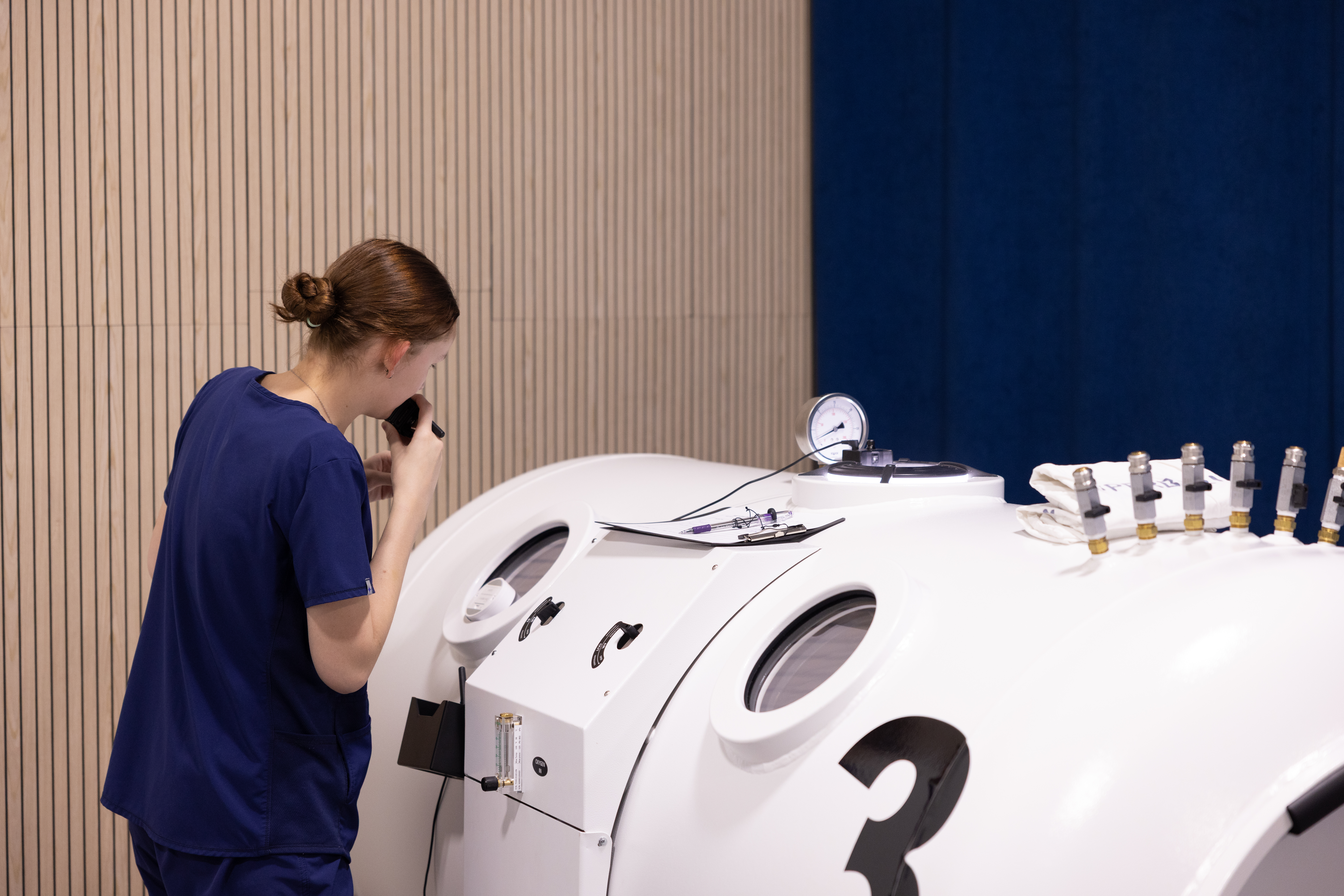 An RX-O2 hyperbaric technician using the chamber communication system beside two chambers