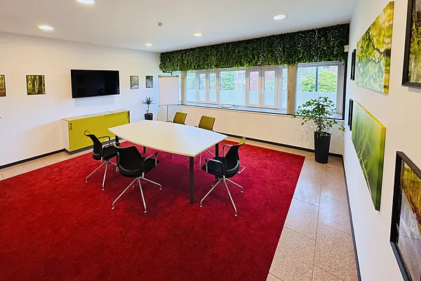 Besprechungsraum mit grüner Pflanzenwand, Tisch und Wandbildschirm
