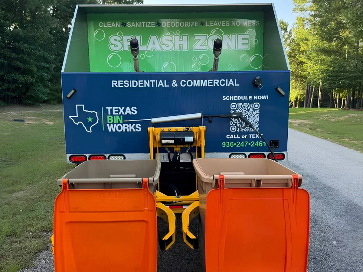 Rear view of a Texas Bin Works trailer with orange bins, showing 'Splash Zone' and contact information on a blue and green design.