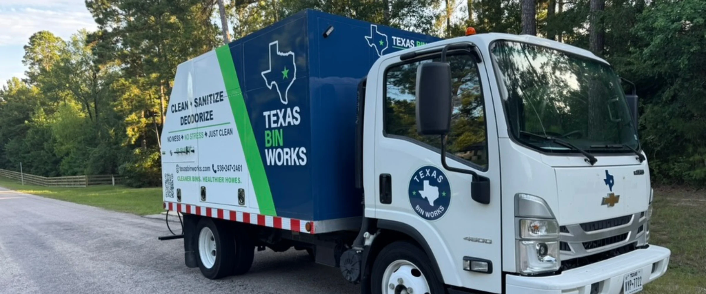 A white Texas Bin Works truck with a blue and green service body parked on a road, advertising bin cleaning services.