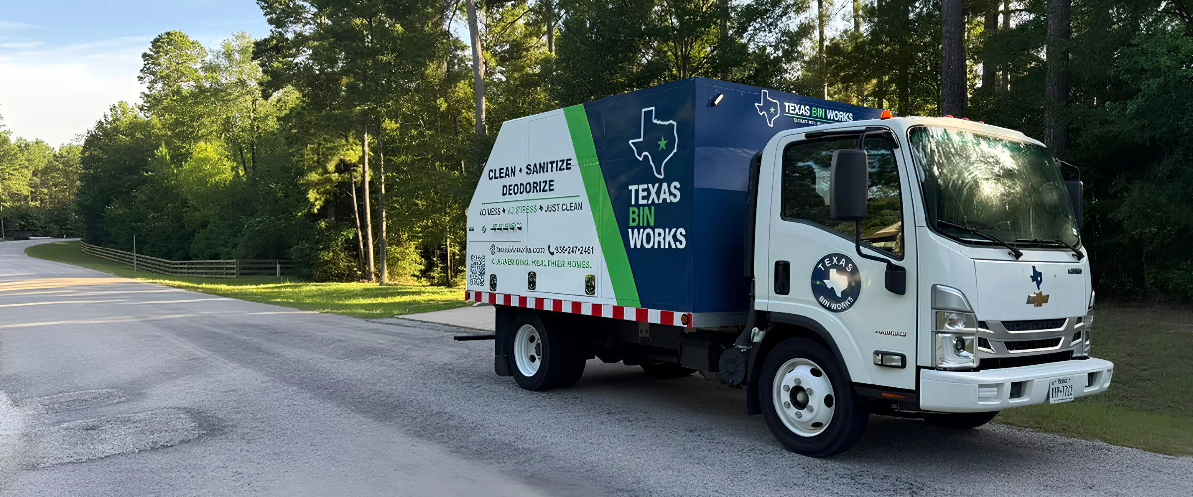 Rear view of a blue Texas Bin Works truck with yellow bin-lifting arms and a reflective bumper on a paved road. Rear view of a blue Texas Bin Works truck with yellow bin-lifting arms and a reflective bumper on a paved road.