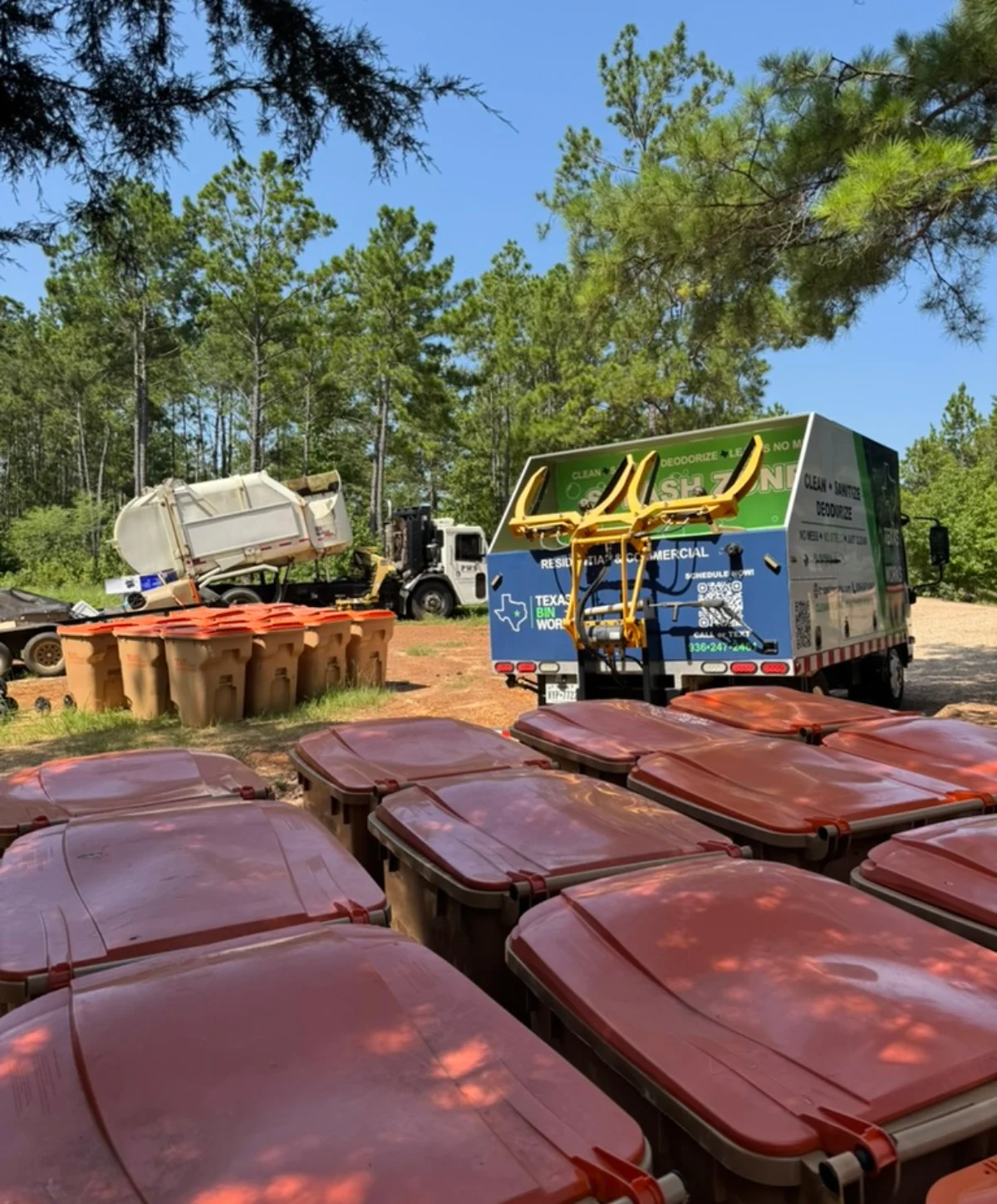 Rows of black trash bins with 'TX Trash It LLC' logos next to a 'Texas Bin Works' cleaning truck on a sunny day.
