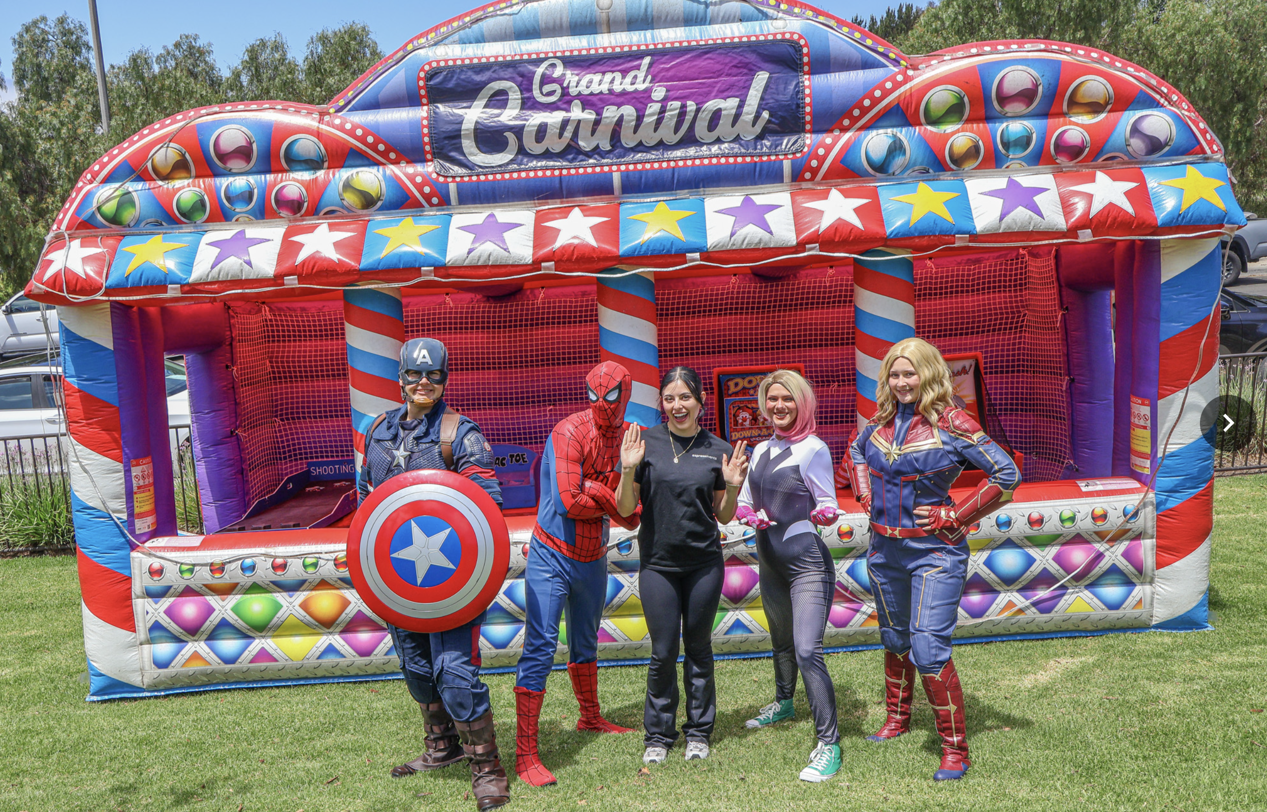 Superhero characters and an Express Events team member in front of the Grand Carnival game package