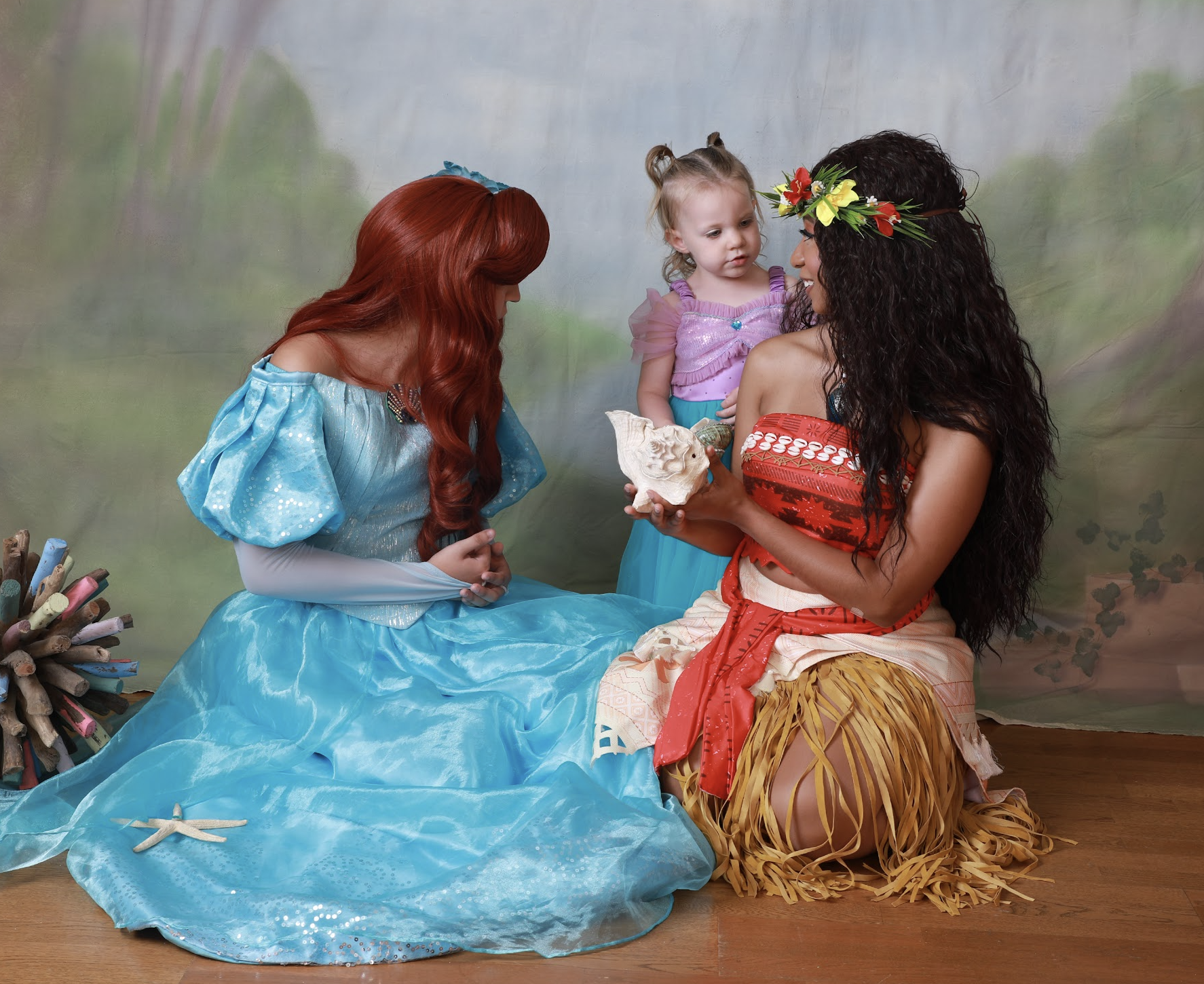 Ariel and Moana sharing a seashell discovery moment with a young guest
