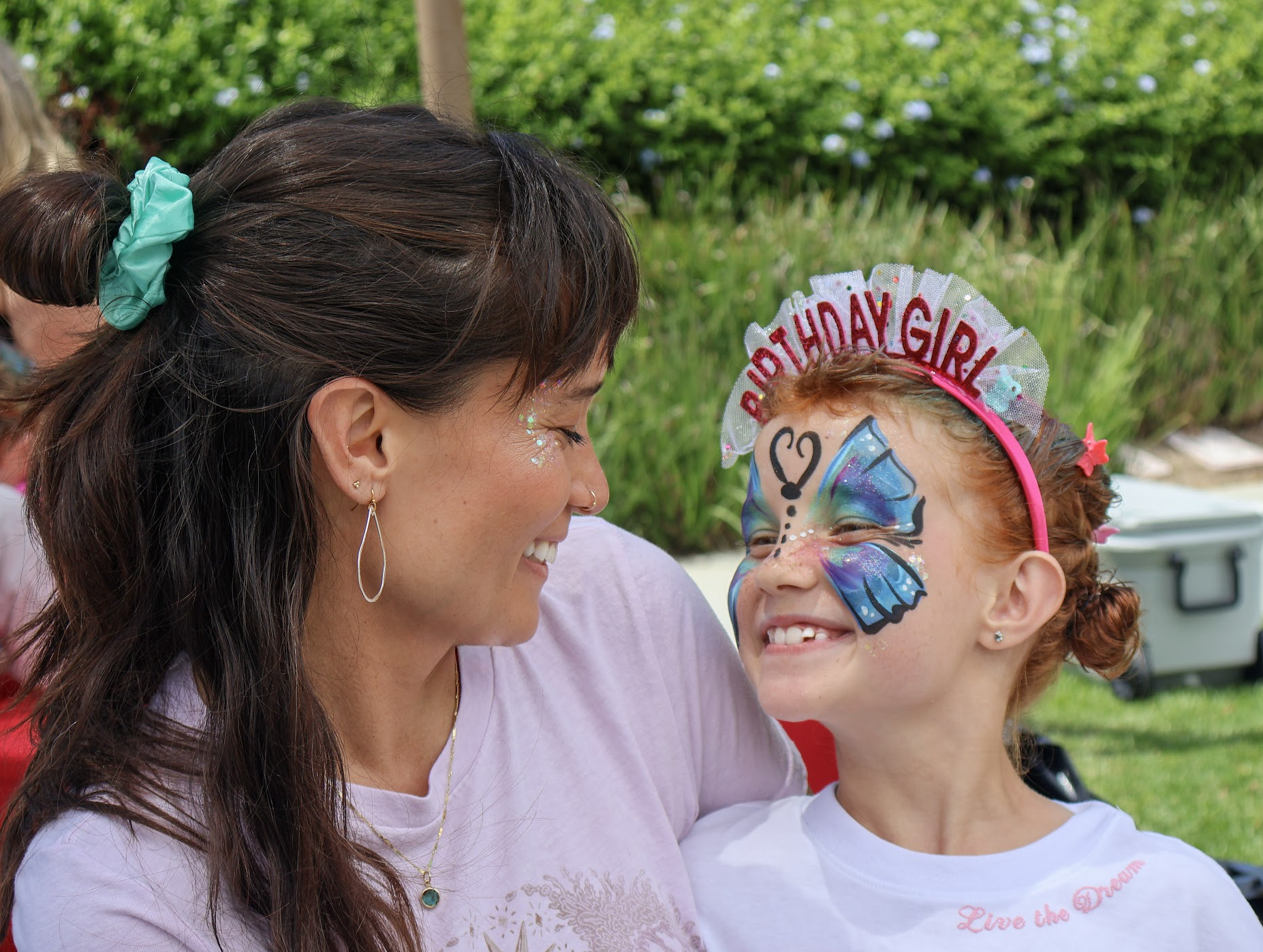 A face painting artist smiling with a birthday child wearing butterfly face art