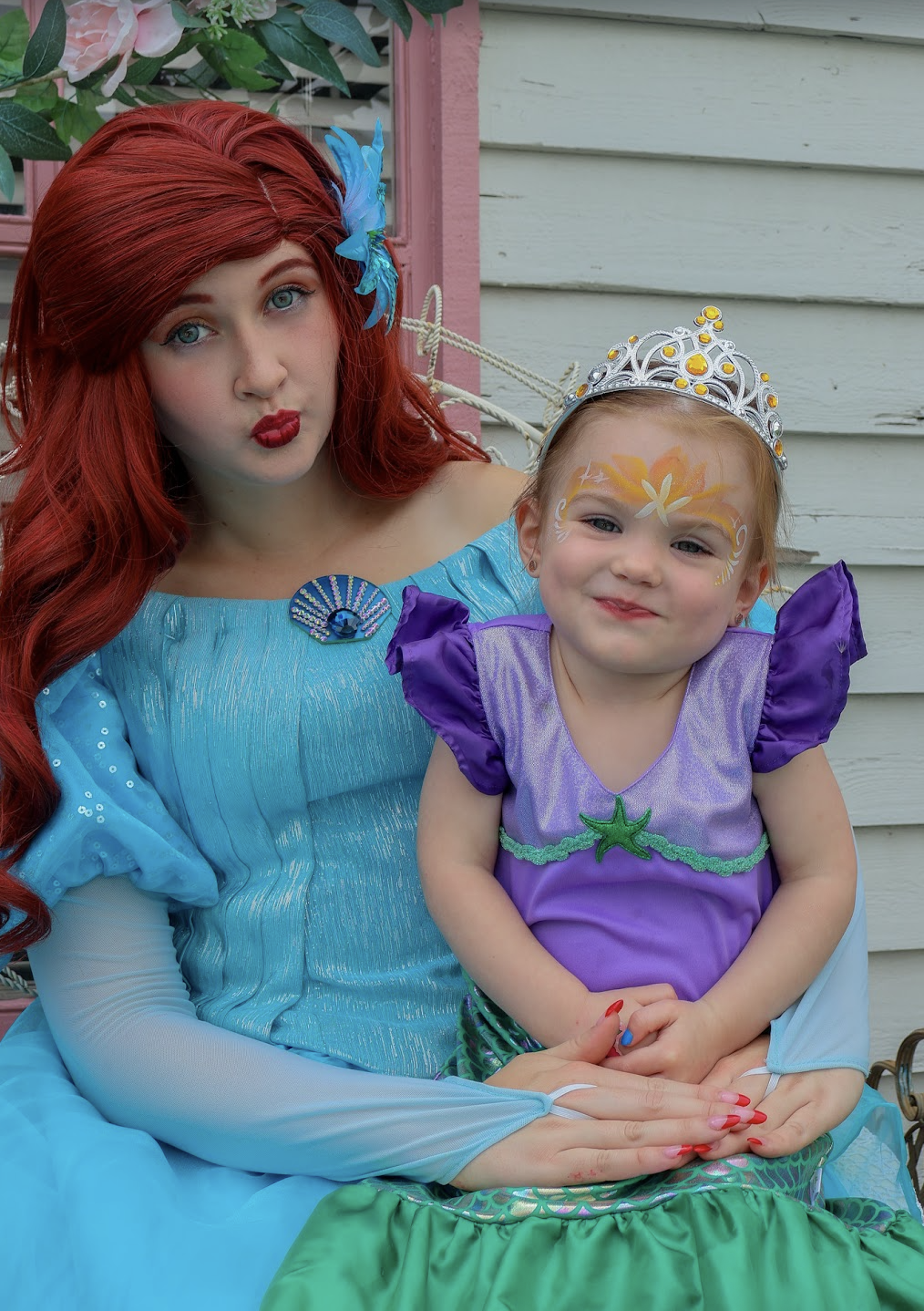 Ariel posing with a young guest wearing a tiara, mermaid dress and face painting