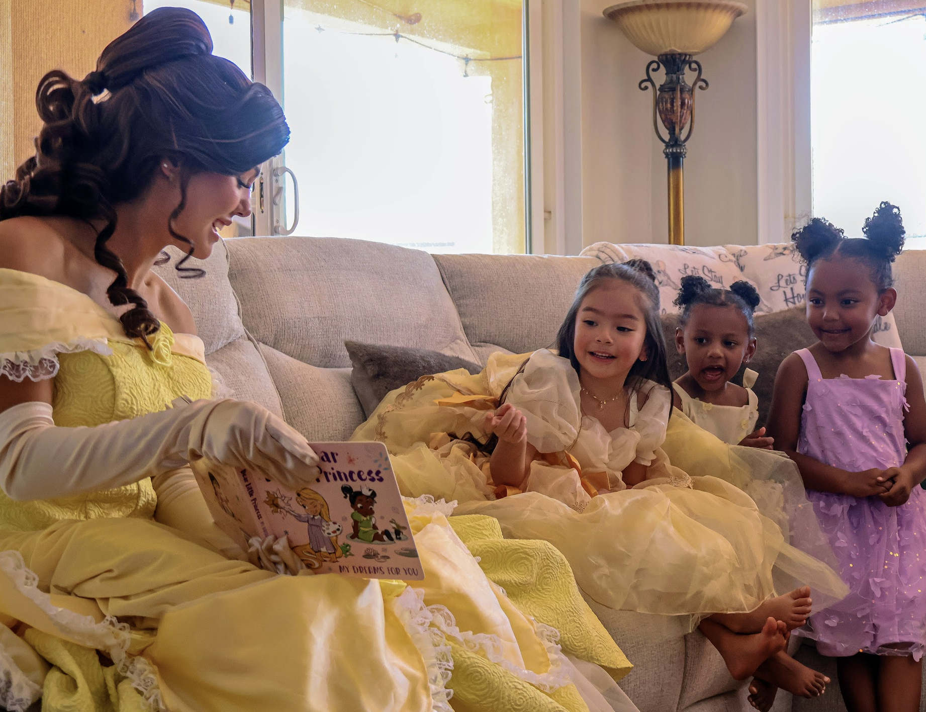 Belle reading a story with three young guests in princess dresses