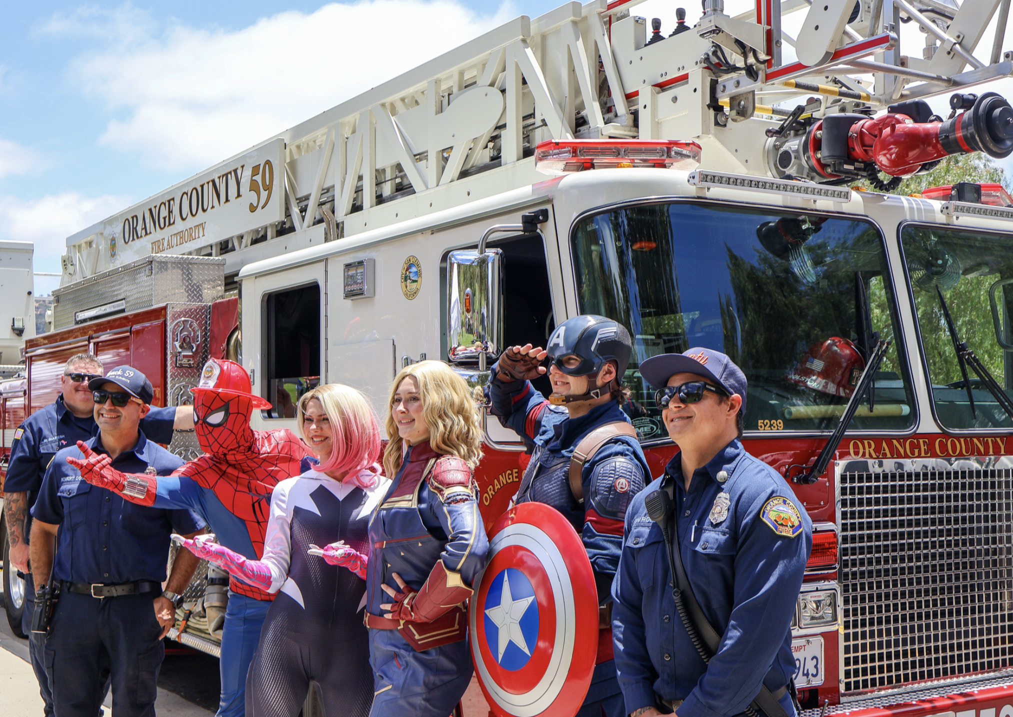 Superhero performers posing with local firefighters beside an Orange County fire truck
