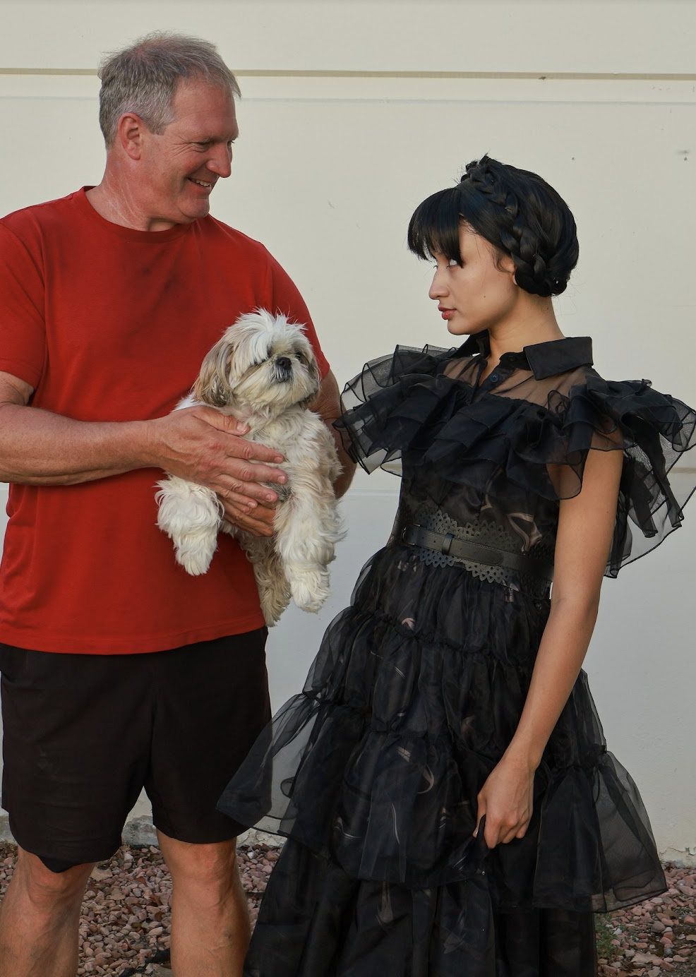 A Wednesday-inspired character sharing a moment with an adult guest holding a small dog