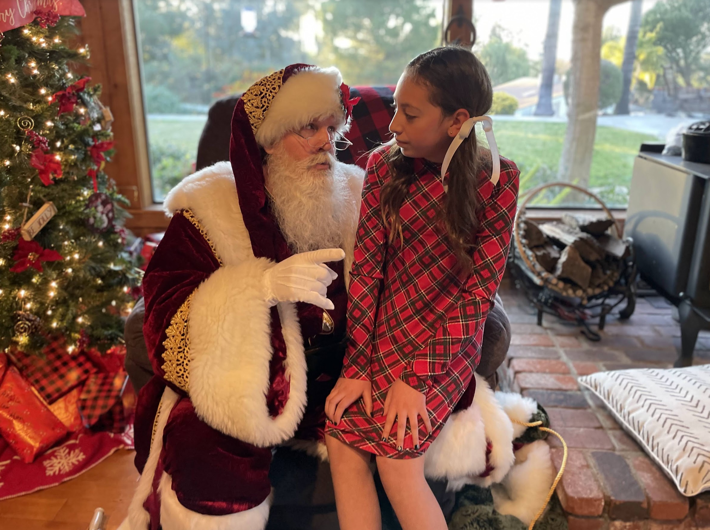 Santa in a burgundy holiday coat sharing a personal moment with a young guest beside a Christmas tree