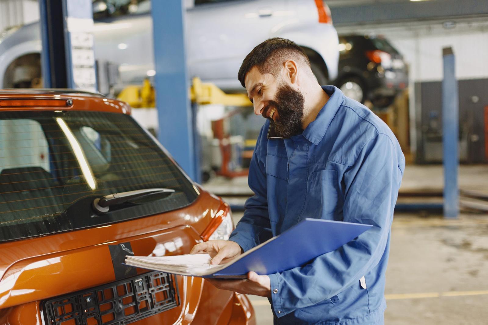 A mechanic in blue overalls smiling while on the phone in a workshop