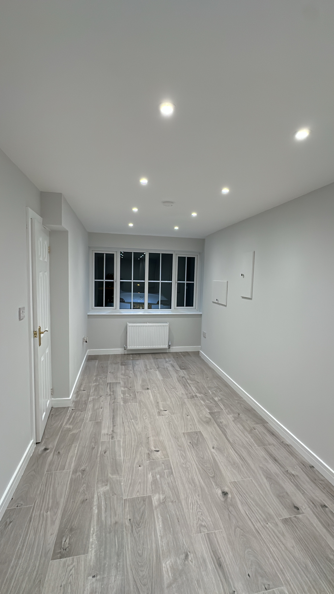 Garage conversion in Radcliffe transformed into a bright additional room with grey wood effect flooring, ceiling spotlights, a radiator and a large front window. Garage conversion in Radcliffe transformed into a bright additional room with grey wood effect flooring, ceiling spotlights, a radiator and a large front window.