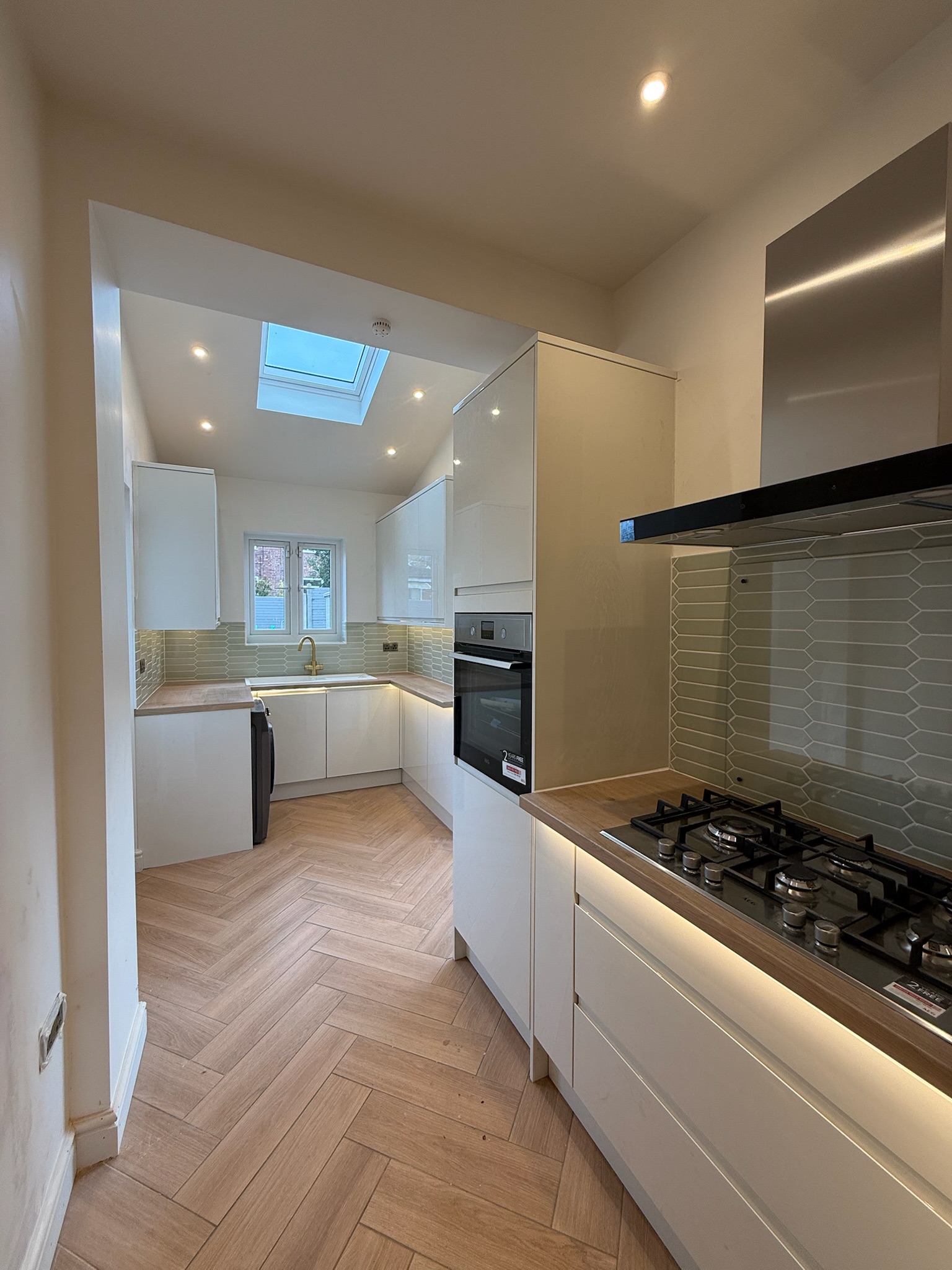 Modern side kitchen extension completed in Stretford featuring skylight, contemporary white kitchen units, herringbone flooring and open plan layout. Modern side kitchen extension completed in Stretford featuring skylight, contemporary white kitchen units, herringbone flooring and open plan layout.