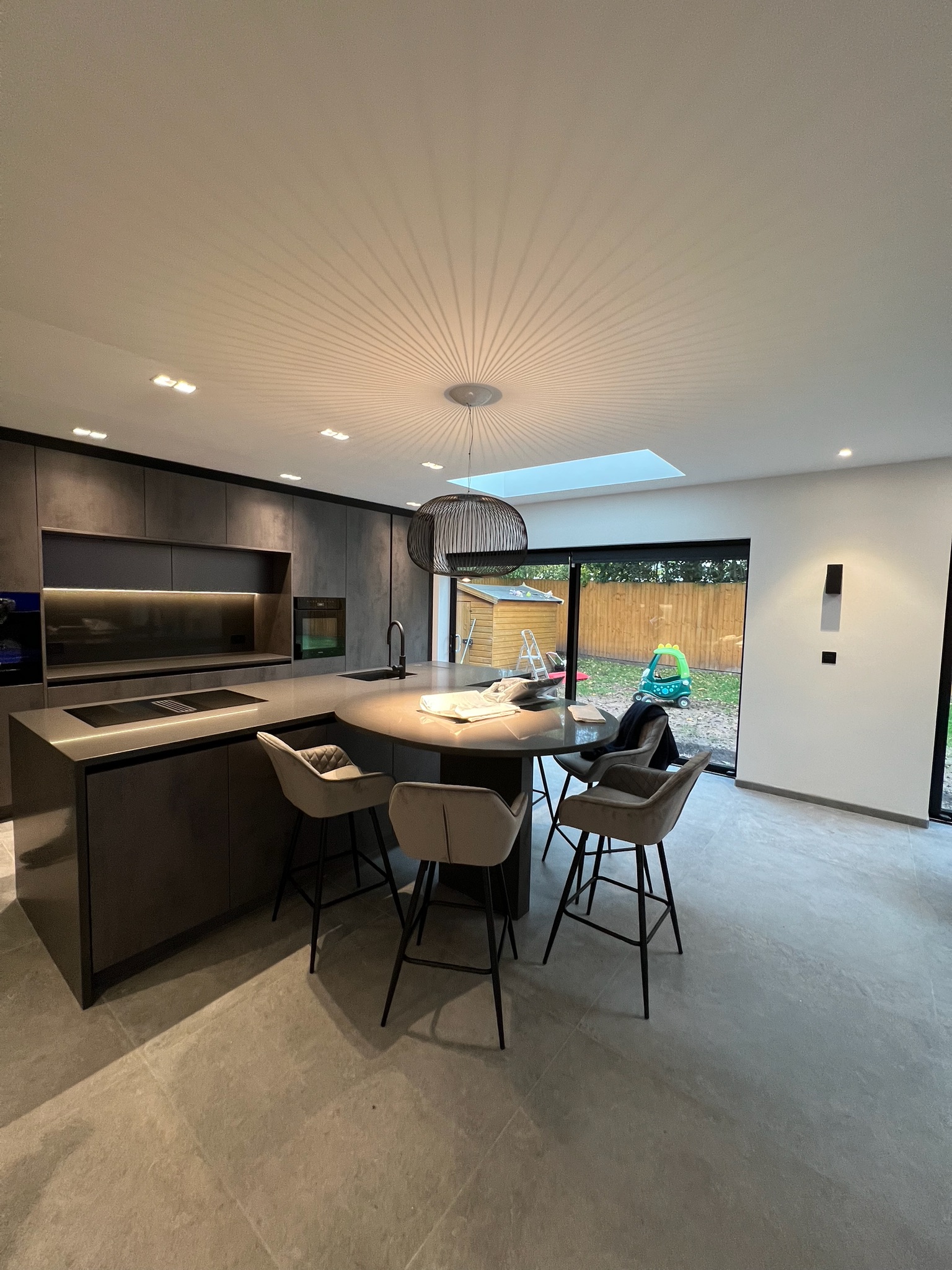 Modern home extension completed in Whitefield featuring contemporary dark kitchen, large island, skylight and open plan living space.