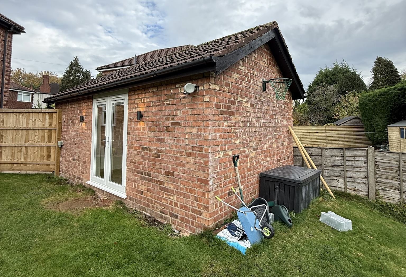 Detached garage conversion in Wilmslow with retained garage storage area and original brick exterior from a side garden angle