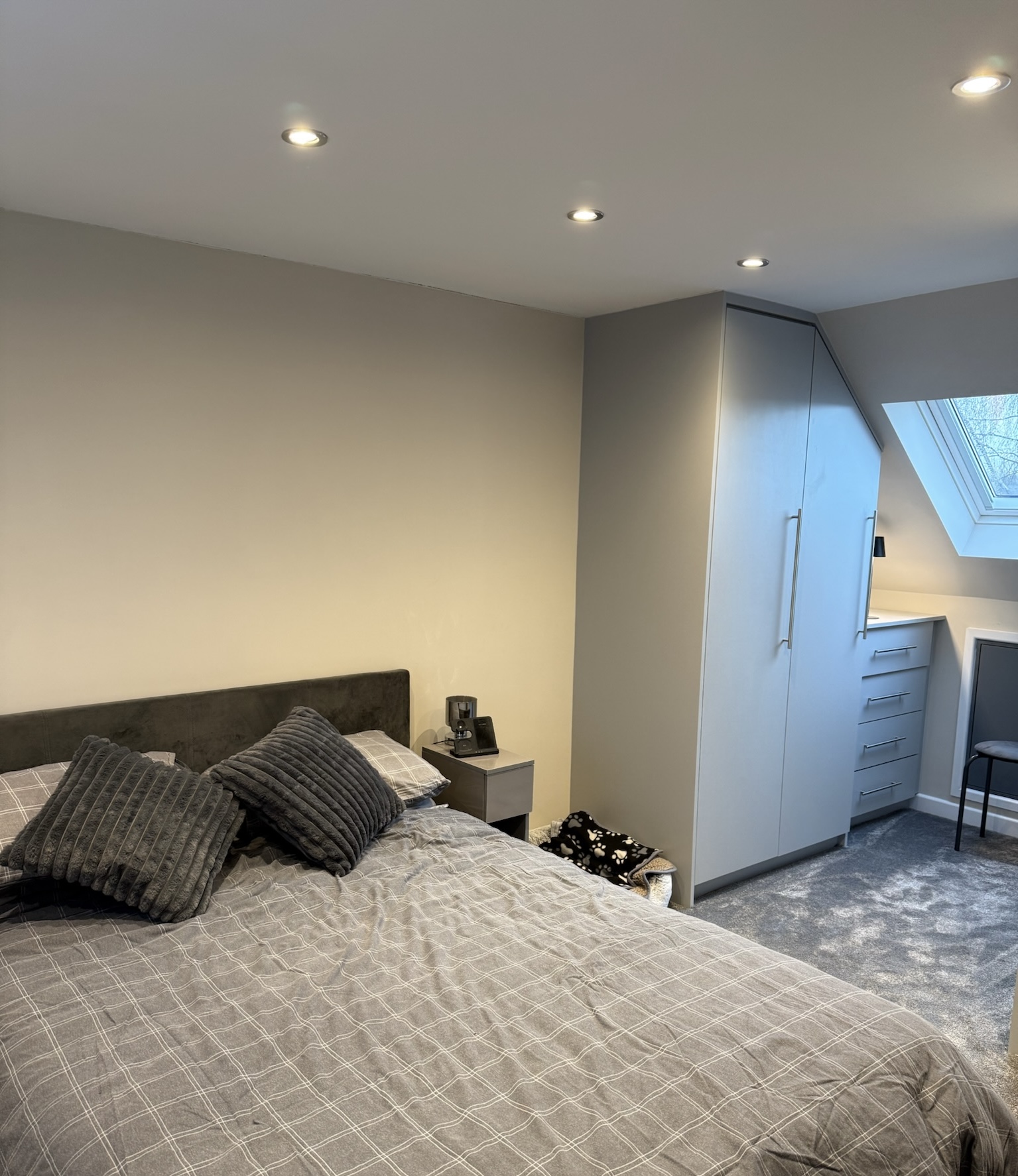 Modern loft conversion bedroom in Whitefield with fitted wardrobes, skylight window, grey carpet and built in storage area