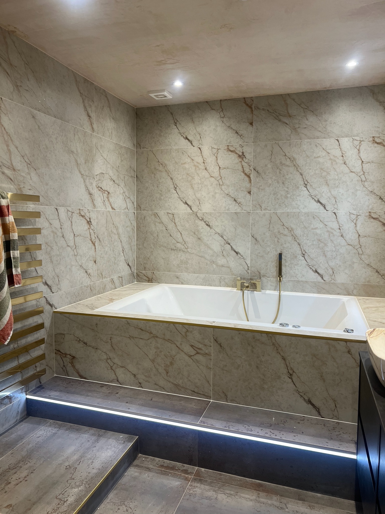Luxury bathroom completed within a home extension featuring marble effect wall tiles, built in bath, LED lighting and brushed brass fittings