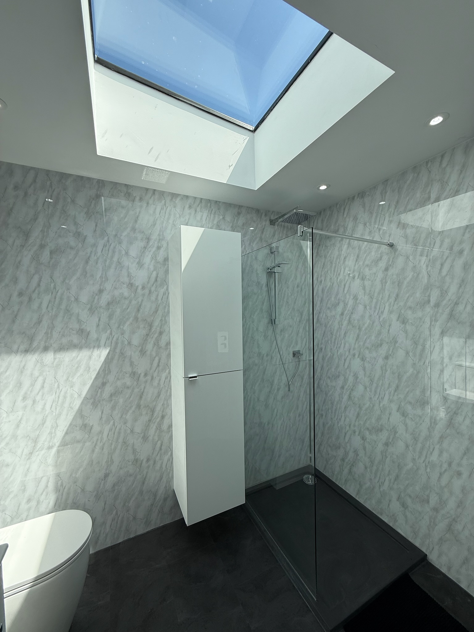 Modern bathroom extension with walk in shower, skylight roof window, marble effect wall panels and minimalist storage design