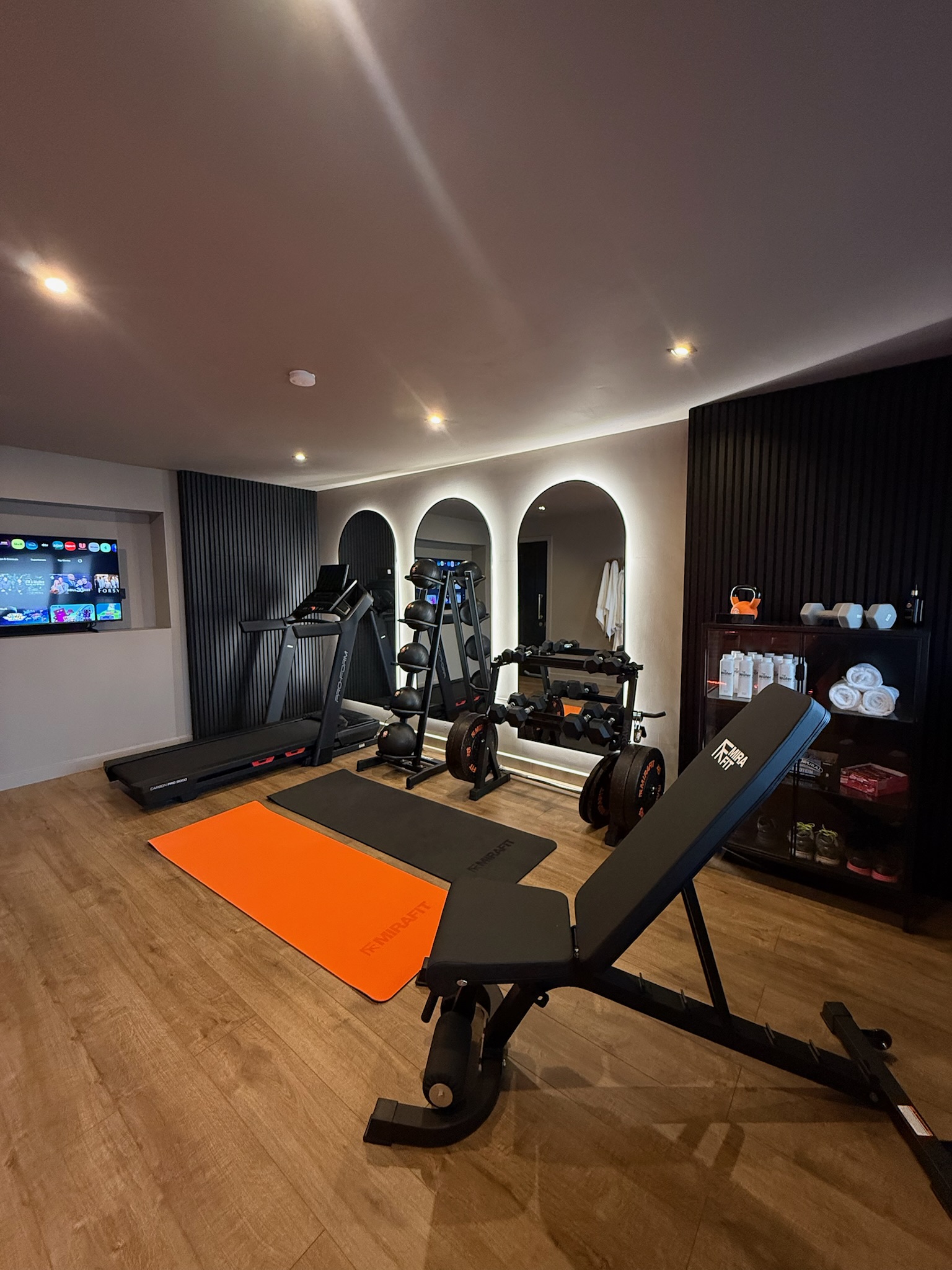 Double garage conversion in Bury transformed into a luxury home gym with treadmill, weight training area, feature mirrors, slatted wall panels and modern lighting. Double garage conversion in Bury transformed into a luxury home gym with treadmill, weight training area, feature mirrors, slatted wall panels and modern lighting.
