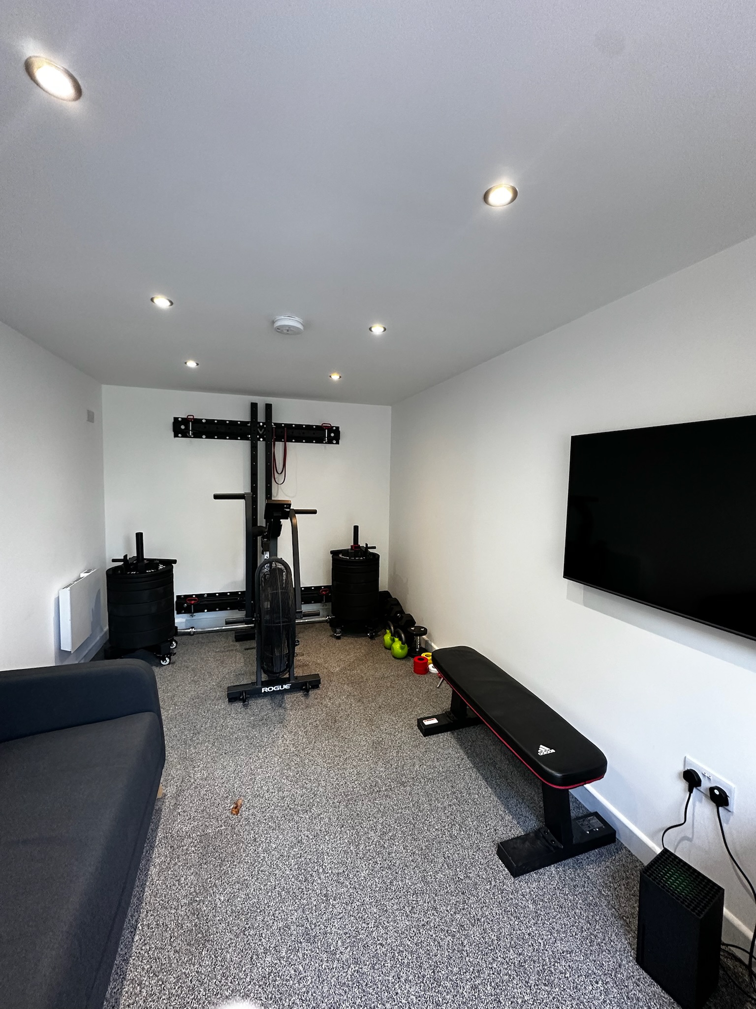 Detached garage conversion in Stockport transformed into a home gym and relaxation space with fitness equipment, wall mounted TV, seating area, insulated flooring and modern recessed lighting. Detached garage conversion in Stockport transformed into a home gym and relaxation space with fitness equipment, wall mounted TV, seating area, insulated flooring and modern recessed lighting.