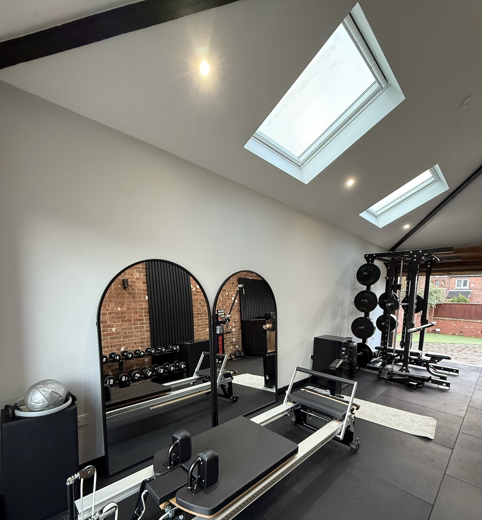 Double garage conversion in Failsworth transformed into a modern home gym with skylights, retained garage door, rubber flooring, strength training equipment and a bright open workout space.