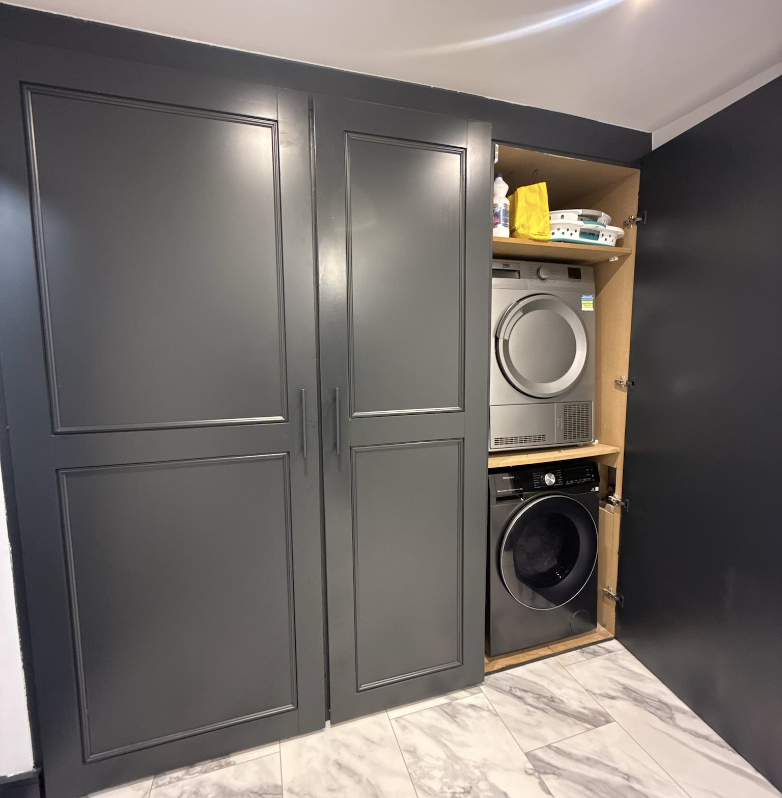Single garage conversion in Rochdale featuring a utility room with built in storage cupboards, stacked washing machine and tumble dryer and fitted cabinetry