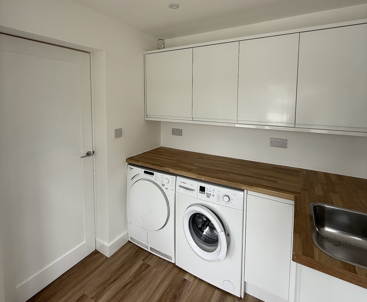 Single garage conversion in Eccles transformed into a practical utility room with fitted storage cupboards, oak worktops, integrated laundry appliances and additional household workspace.