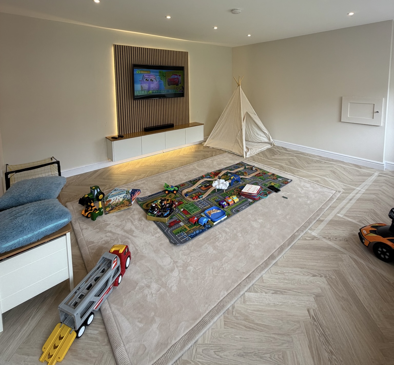 Double garage conversion in Bolton transformed into a spacious children's playroom with herringbone flooring, fitted storage, feature slatted TV wall, soft play area and plenty of open floor space for family living.
