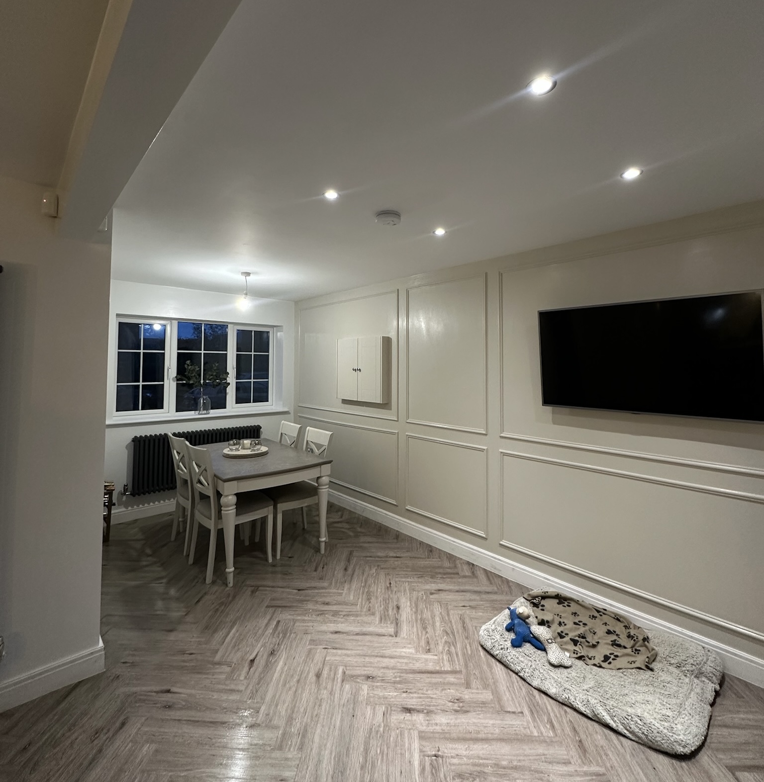 Open plan kitchen and dining area created through a garage conversion with herringbone flooring, wall panelling and recessed ceiling spotlights.