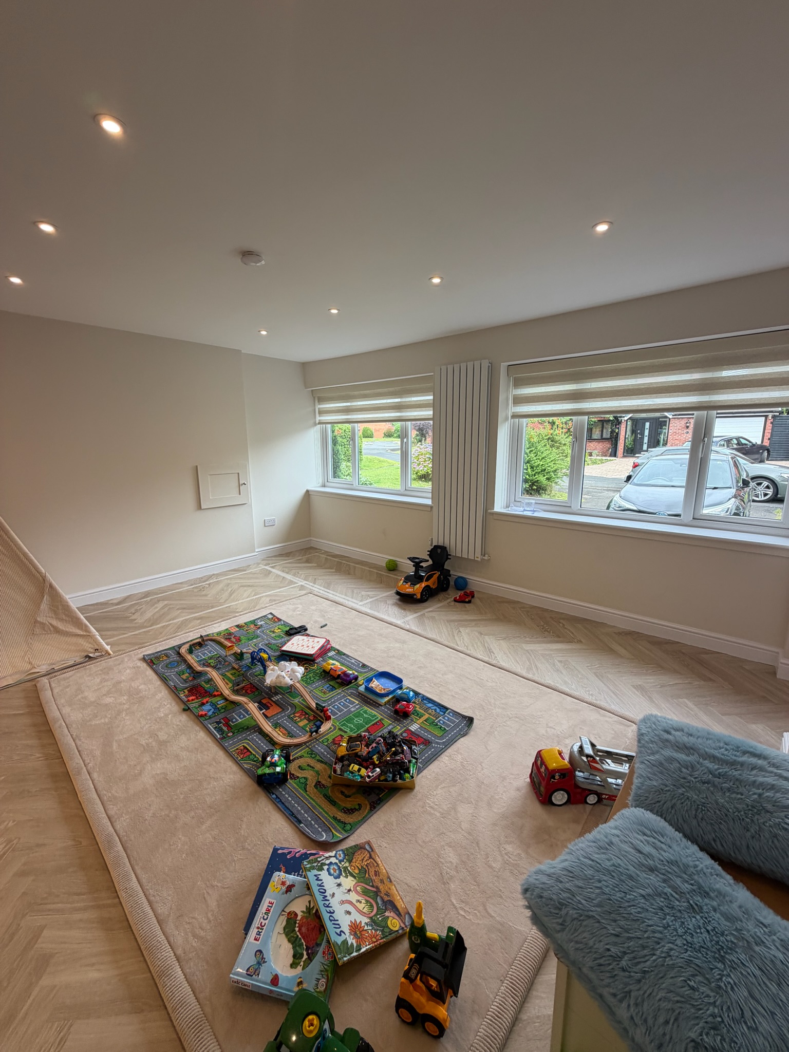 Double garage conversion in Bolton transformed into a spacious children's playroom with large front windows, herringbone flooring, recessed lighting and plenty of open floor space for toys, games and family activities.