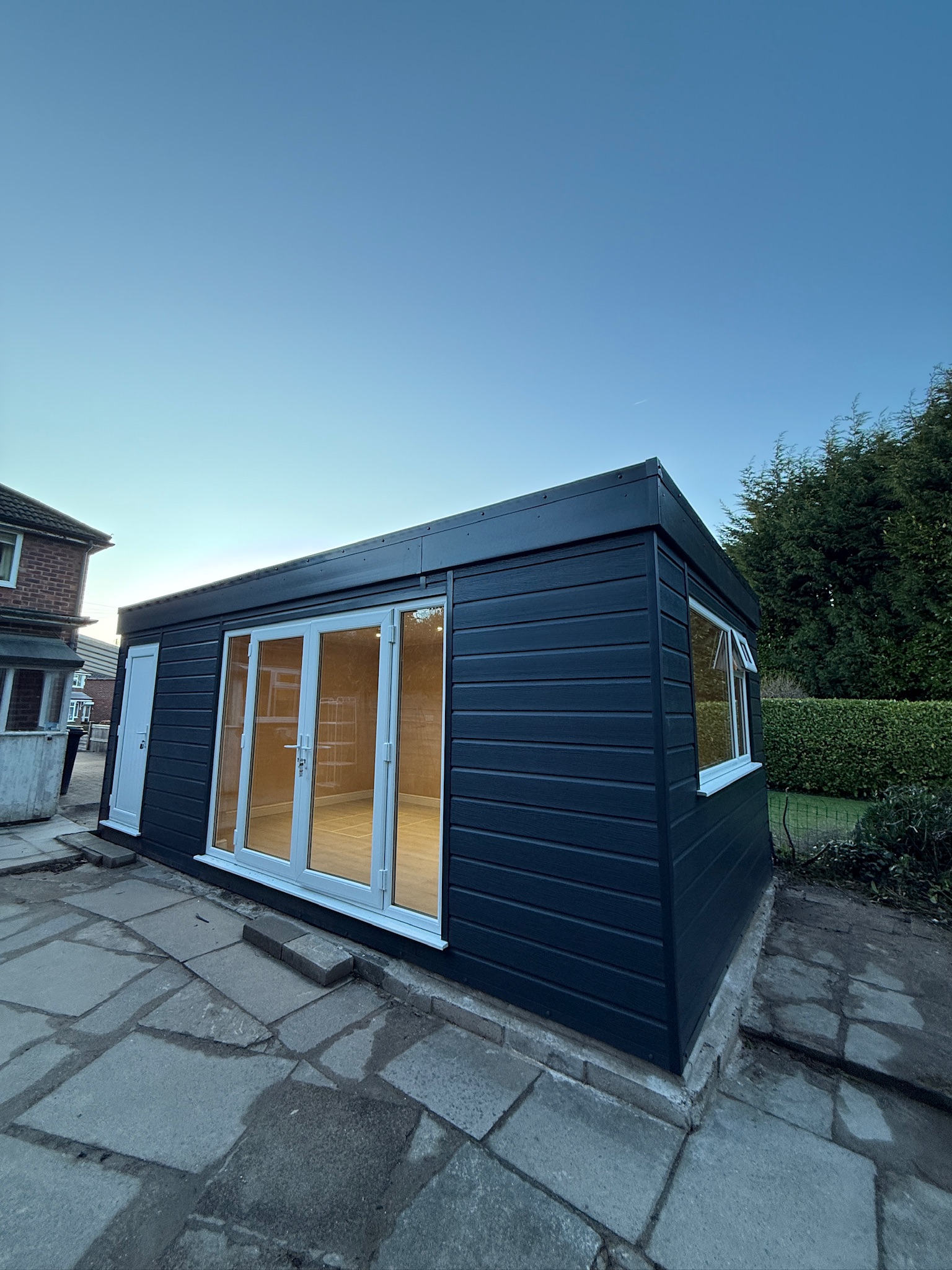 Completed garage conversion in Wilmslow showing the renovated exterior with dark cladding, new French doors, windows and a separate entrance. Completed garage conversion in Wilmslow showing the renovated exterior with dark cladding, new French doors, windows and a separate entrance.