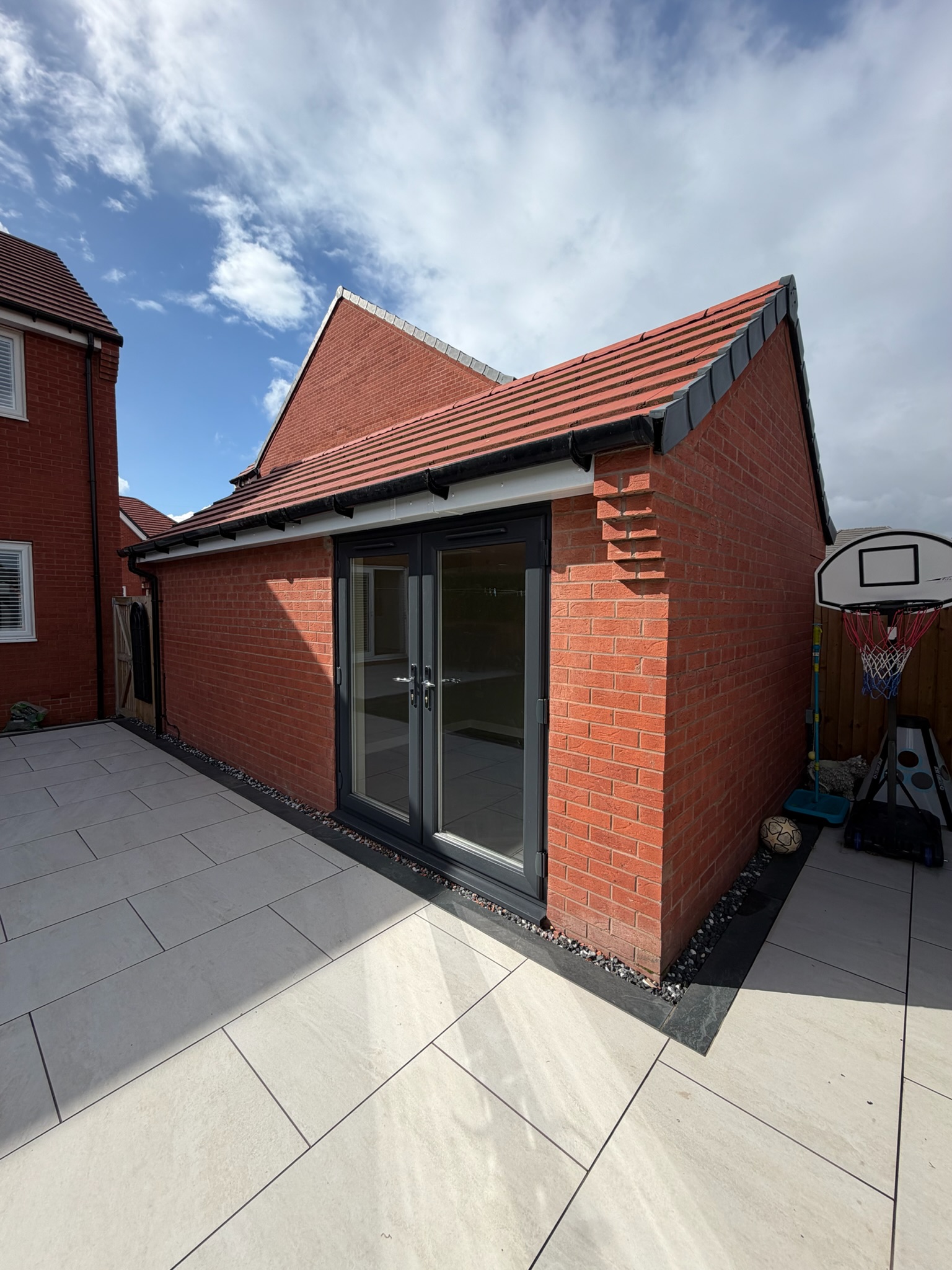 Detached single brick garage conversion in Atherton with a pitched tiled roof, black glazed double doors and paved garden access.