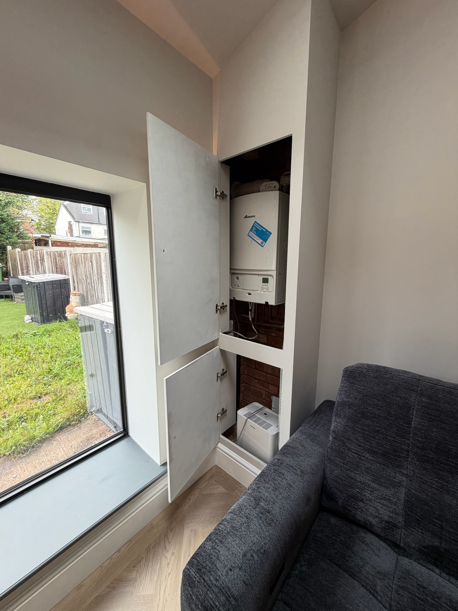 Single garage conversion in Crewe transformed into a living room, featuring a fitted cupboard housing an existing boiler beside a large window. Single garage conversion in Crewe transformed into a living room, featuring a fitted cupboard housing an existing boiler beside a large window.