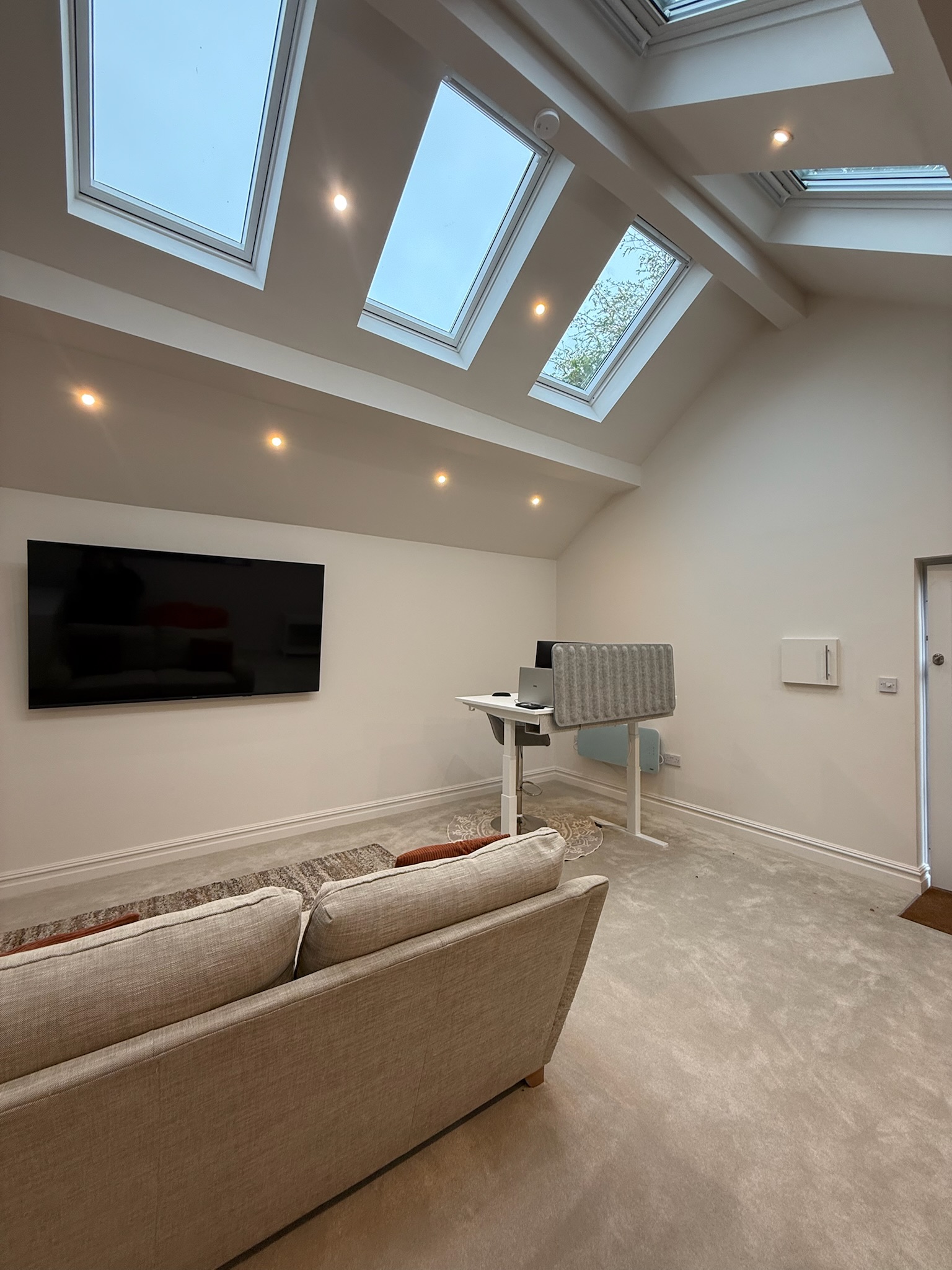 Double garage conversion in Atherton transformed into a cinema room and office with vaulted ceiling, rooflights, wall mounted television, sofa and recessed spotlights.
