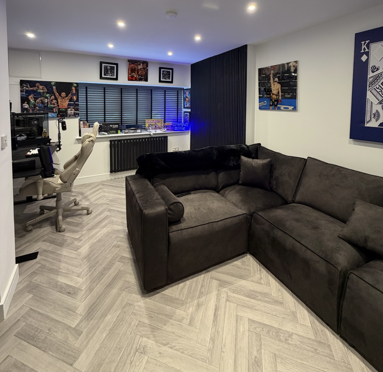 Alt text: Single garage conversion in Middleton transformed into a games room with gaming desk, large corner sofa, feature wall and herringbone flooring. Alt text: Single garage conversion in Middleton transformed into a games room with gaming desk, large corner sofa, feature wall and herringbone flooring.