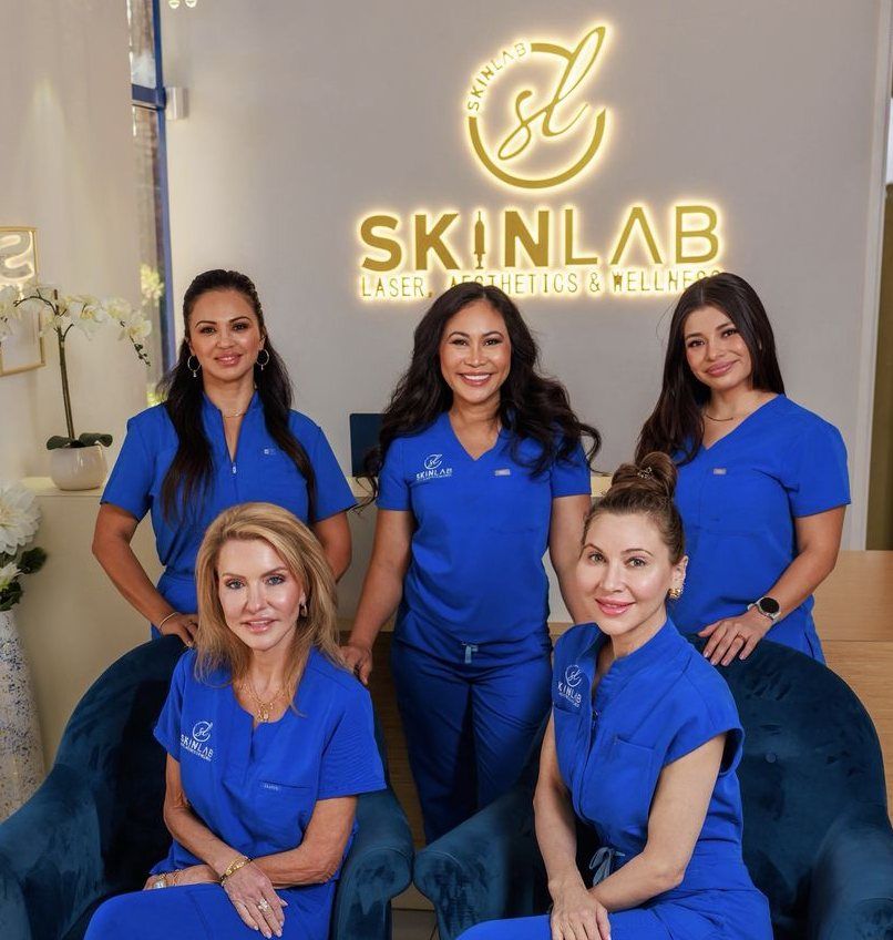 The SkinLab team seated and standing in front of the glowing SkinLab sign