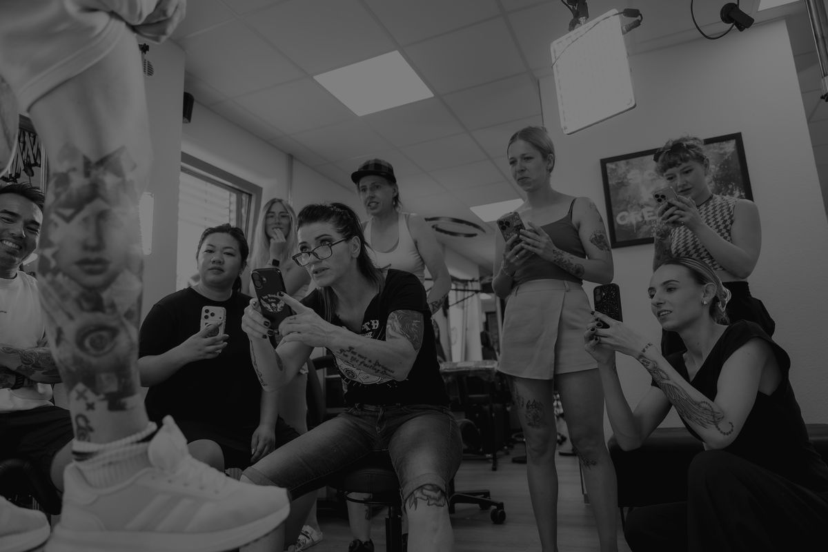 Teilnehmer filmen im Workshop ein frisch abgeheiltes Bein-Tattoo