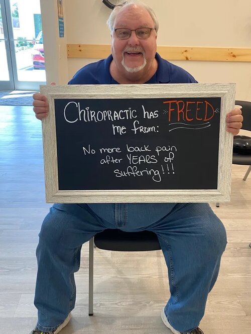 A man with glasses holding a chalkboard sign about relief from years of back pain at Lake Nona Chiropractic