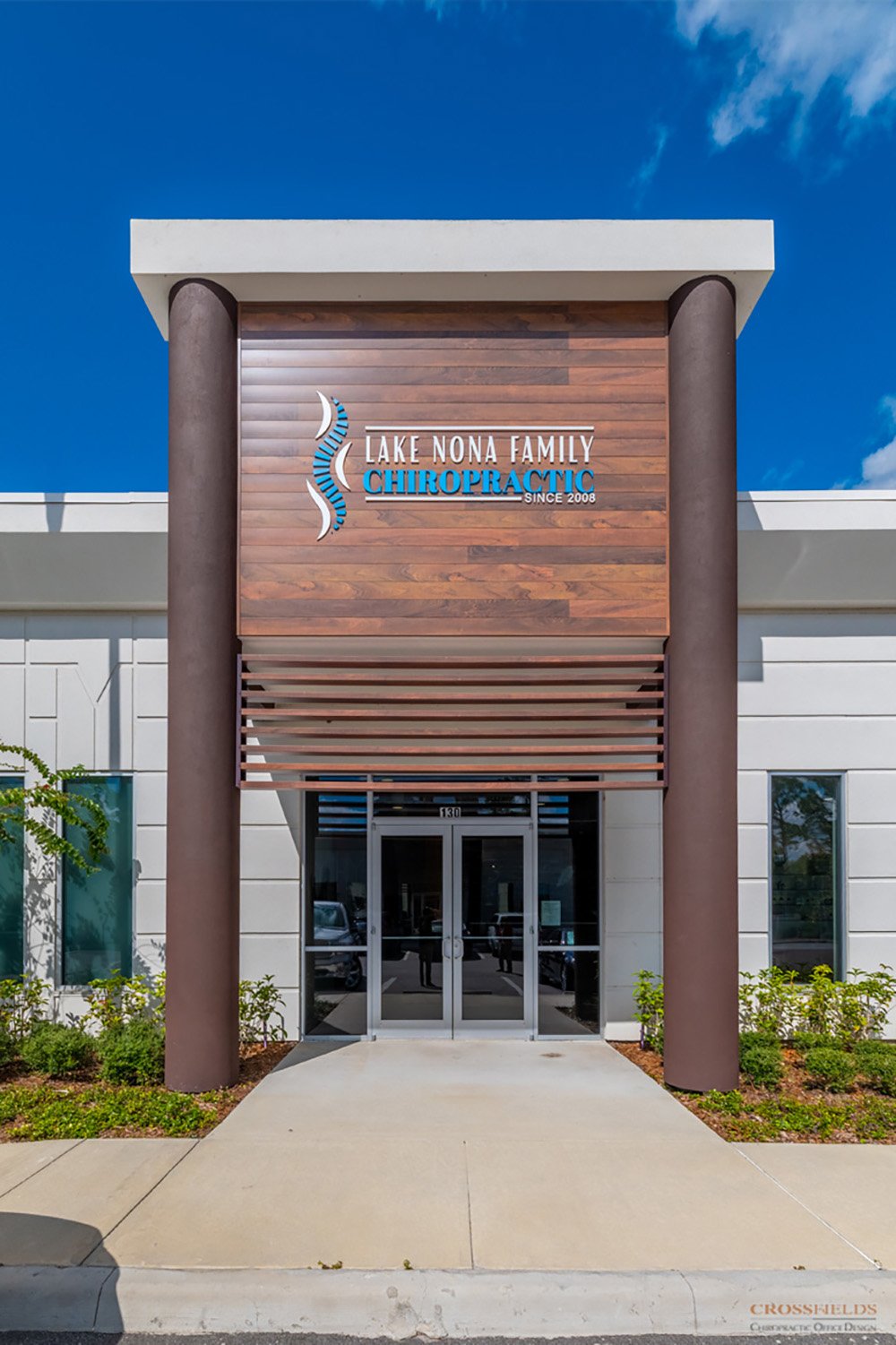 Front view of Lake Nona Chiropractic building with wooden and white exterior, two brown columns, and a glass door entrance.