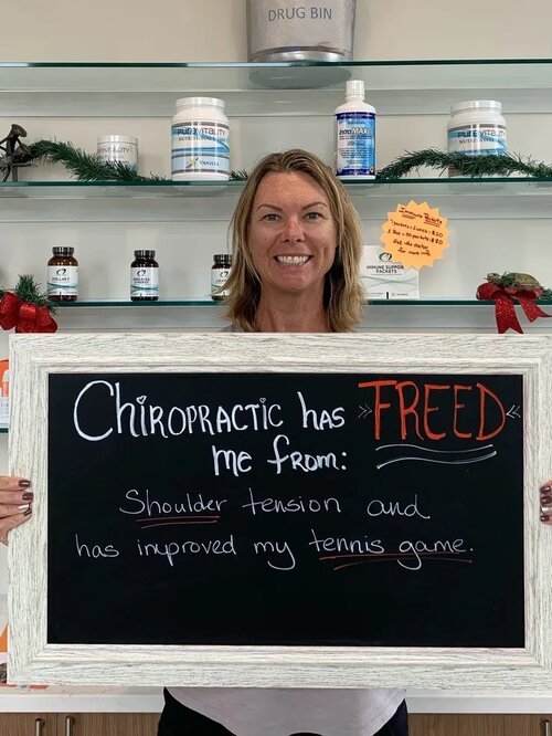 A woman holding a chalkboard sign about relief from shoulder tension and improved tennis game at Lake Nona Chiropractic