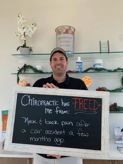 A smiling patient holding a chalkboard sign sharing their experience at Lake Nona Chiropractic