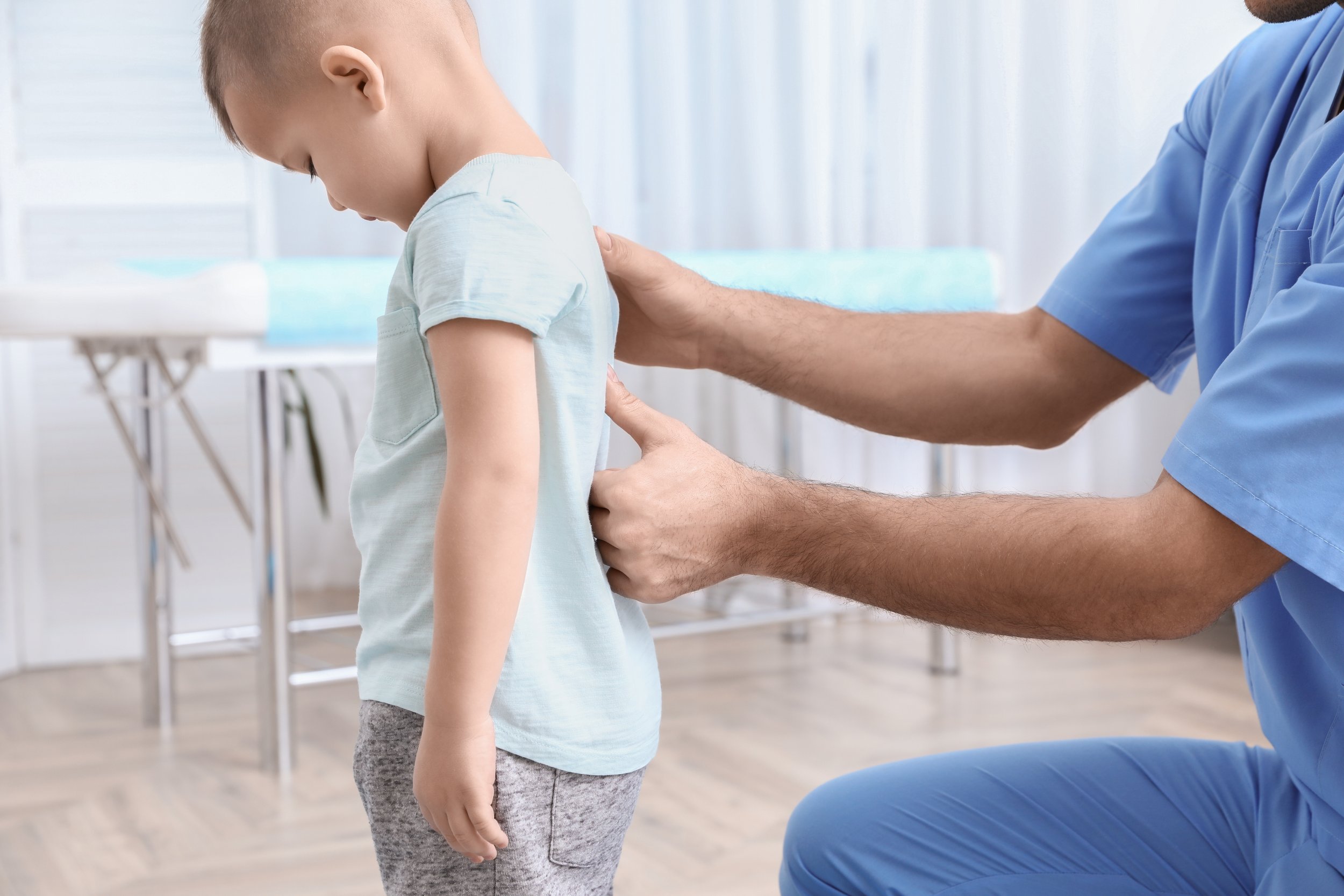 Doctor examining a young patient's back during a ScoliBrace follow-up visit in the office