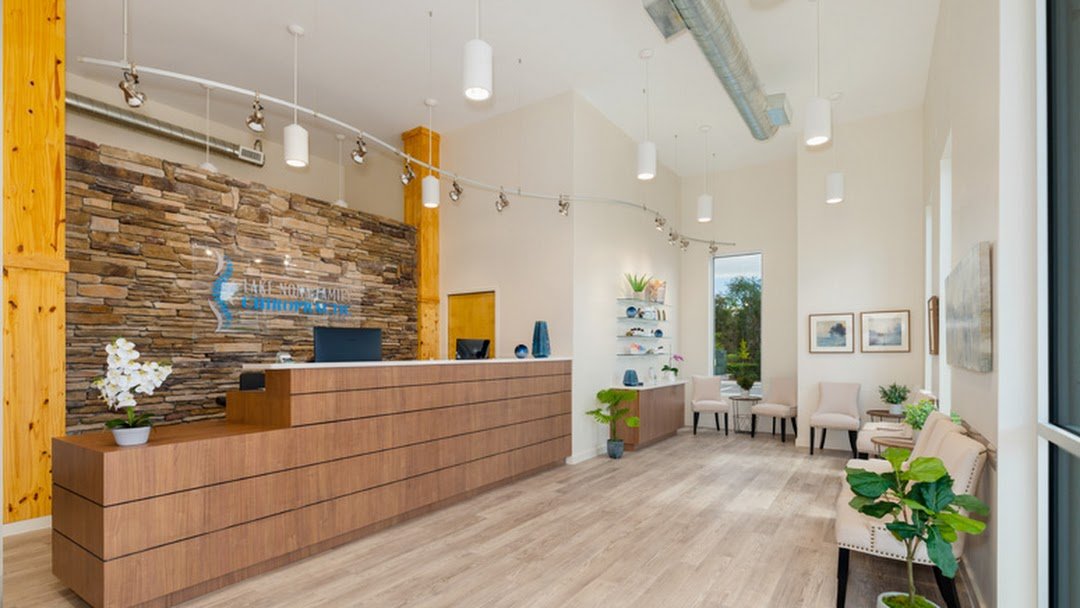 Modern reception area with wooden desk, stone accent wall, white chairs, potted plants, and wall art.