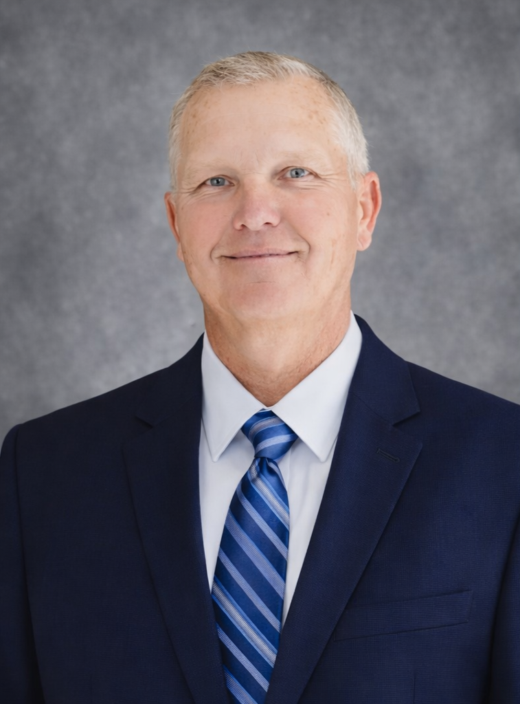 Headshot of Dr. Frank Berzanskis Sr., founder of Lake Nona Chiropractic, wearing a navy blue suit, white shirt, and blue striped tie, smiling against a gray textured background.