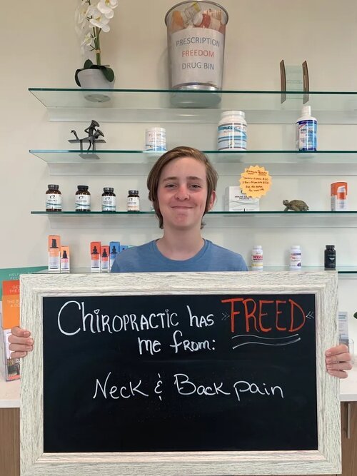 A young woman holding a chalkboard sign about relief from neck and back pain at Lake Nona Chiropractic