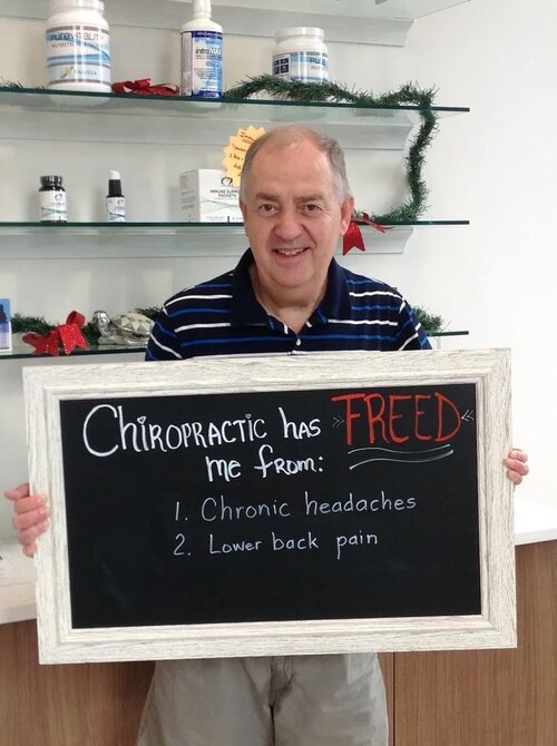 A man holding a chalkboard sign about relief from chronic headaches and lower back pain at Lake Nona Chiropractic